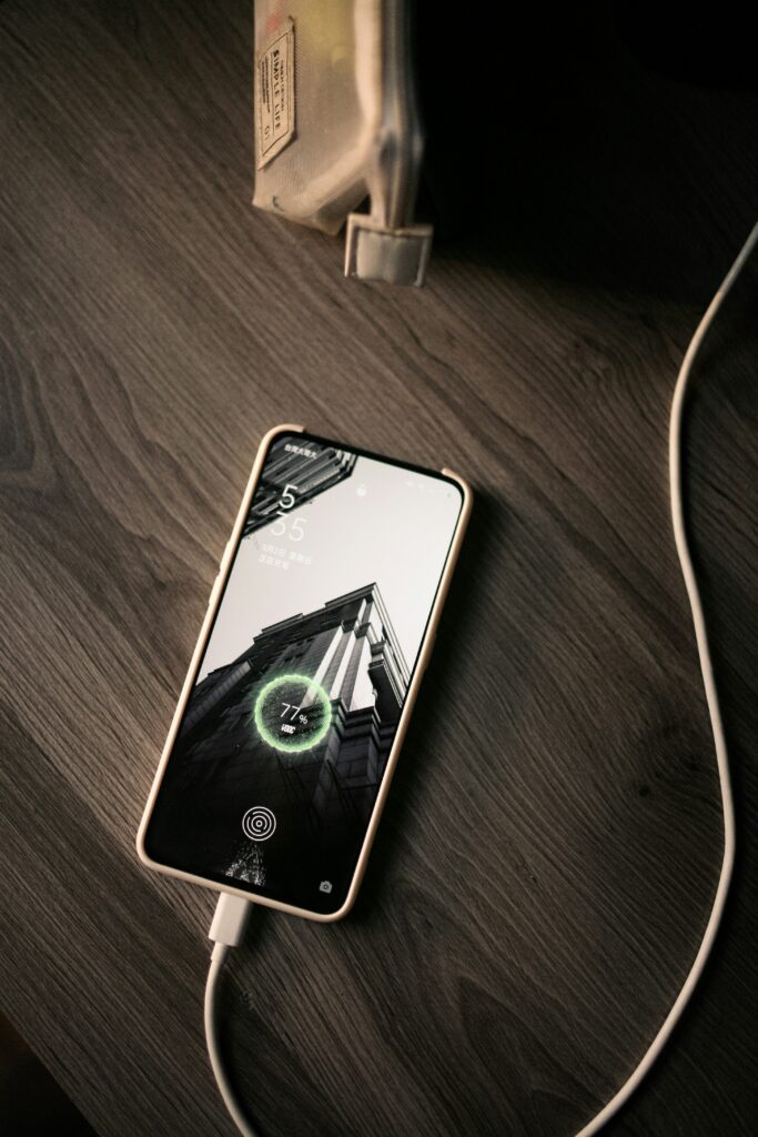 Smartphone charging on wooden table showing battery percentage