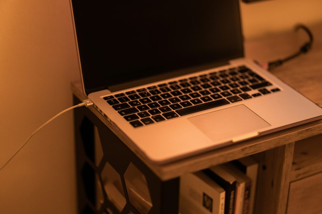 Laptop charging on a wooden desk under warm lighting